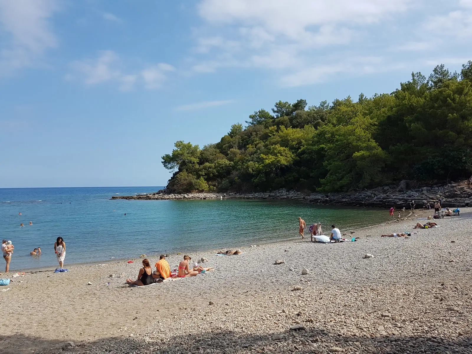 Pebble cove beach and swimmers beside Phaselis archaeological site